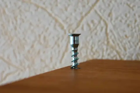 A metal screw is stuck in a wooden surface. This image might be useful for a guide on how to remove stuck screws.