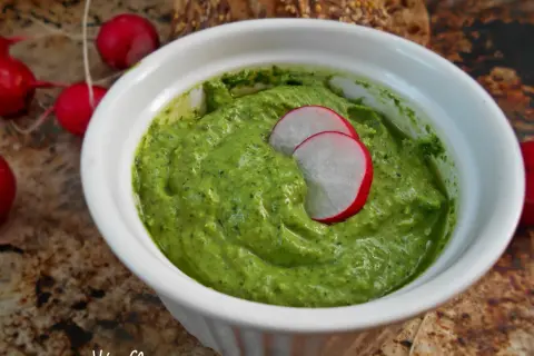 Zielone pesto z liści rzodkiewki w białej miseczce, ozdobione plasterkami rzodkiewki.