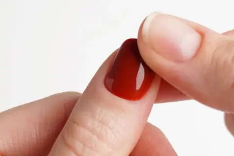 Dita che applicano unghie finte rosse, mostrando come attaccare le unghie finte senza colla con adesivi.
