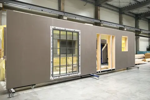 Gotowe ściany drewniane prefabrykowane z oknami i otworami na drzwi, czekające na montaż.