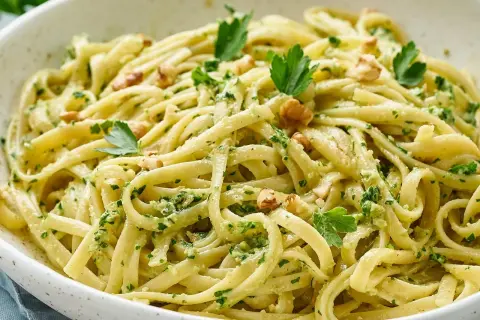 Pasta con pesto cremosa, adornada con nueces y perejil fresco. Un plato italiano delicioso y vibrante.