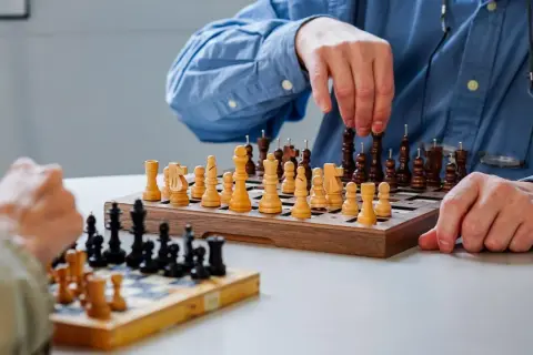 Deux personnes jouent aux échecs. Les pièces ont des ergots pour aider à les identifier, rendant ce jeu accessible aux aveugles.