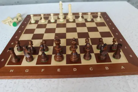 Ułożenie pionków w szachach. Drewniana szachownica z ciemnymi i jasnymi figurami, gotowa do gry.