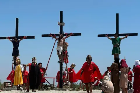 Nachstellung, wie Jesus stirbt am Kreuz, mit zwei weiteren Männern, die ebenfalls gekreuzigt werden. Soldaten in römischer Kleidung und Zuschauer sind anwesend.