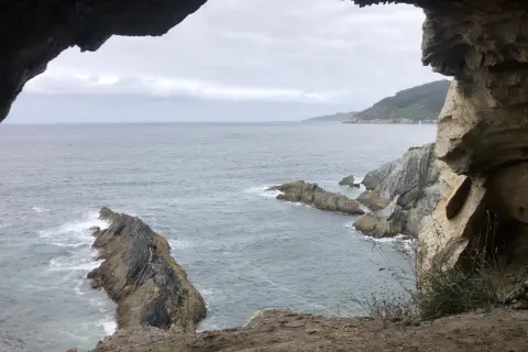 Vista desde la cova da doncela. El mar agitado choca contra las rocas mientras una vela solitaria navega en el horizonte.