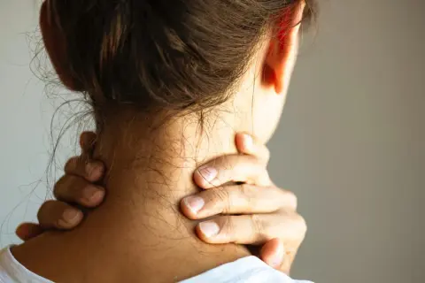 Frau greift sich an den Nacken, um einen steifen Nacken zu lindern. Was hilft sofort? Sanfte Dehnung und Wärme können Linderung bringen.
