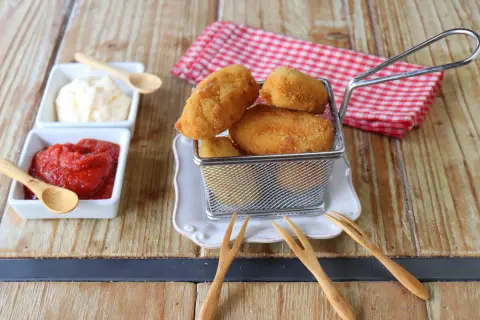 Croquetas de gambas doradas y crujientes en una cesta metálica, acompañadas de ketchup y mayonesa.