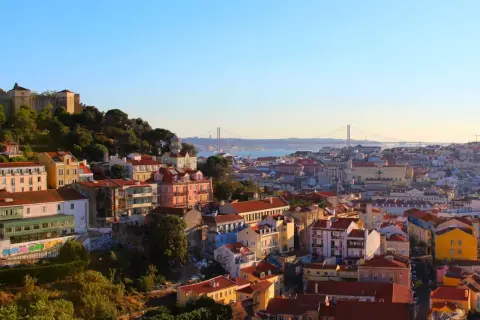 Vy över Lissabon med färgglada hus och en bro i fjärran. Perfekt för lissabon shopping och att uppleva stadens charm.
