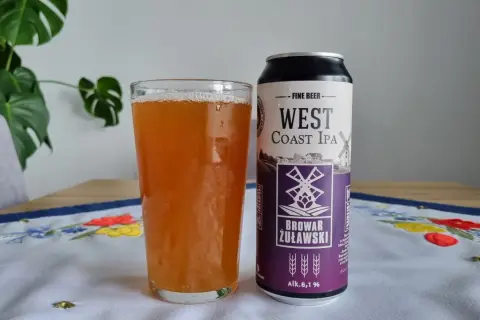 Szklanka piwa West Coast IPA obok puszki Browaru Żuławski. Na obrusie haftowane kwiaty.