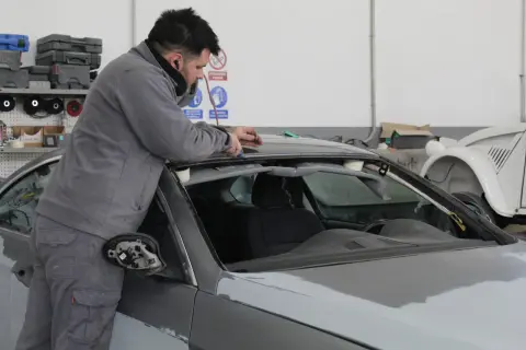 Taller mecánico. Un hombre trabaja en el techo de un coche gris, solucionando stage 1 problemas.