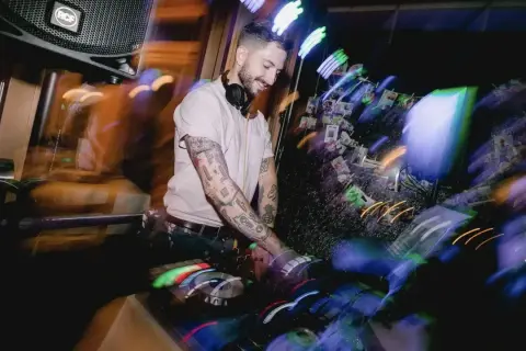 Ein guter DJ mit tätowierten Armen legt Musik auf, während bunte Lichter die Szene in Bewegung setzen.