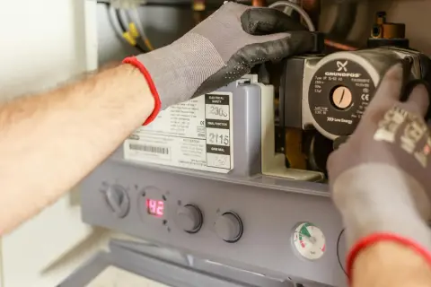 Ręce w rękawiczkach pracują przy budowie bojlera elektrycznego, regulując pompę Grundfos.
