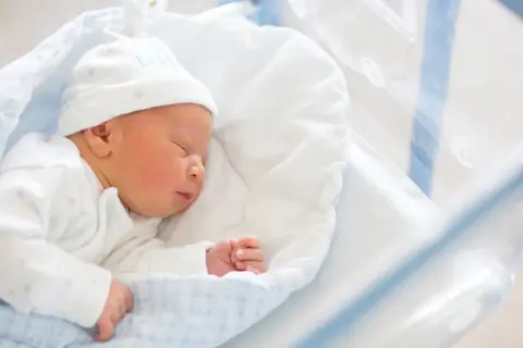 Śpiące noworodek w szpitalnym łóżeczku. Dowiedz się, jak wypełnić wniosek o becikowe, by zapewnić mu najlepszy start.