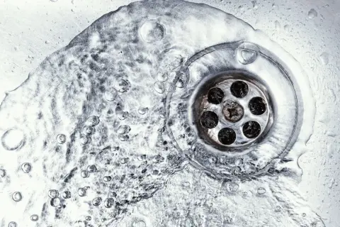 Wasser fließt in einen verstopften Abfluss. Vielleicht hilft ein Gebissreiniger, die Ablagerungen zu lösen.