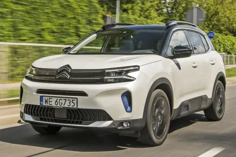 Biały Citroen C5 Aircross 2025 z czarnym dachem pędzi po drodze, otoczony zielenią.