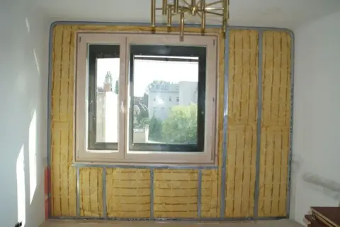 Izolacja akustyczna wokół okna, z widocznym materiałem w kolorze piaskowym na ścianie, przygotowana do dalszych prac wykończeniowych.