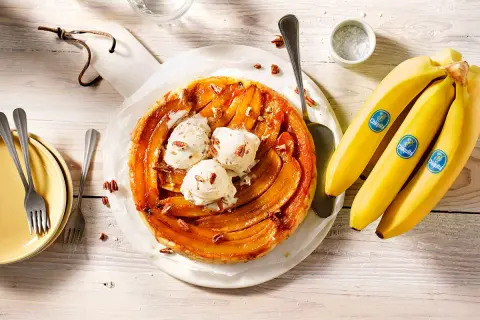 Eine köstliche gebackene Banane Tarte mit Vanilleeis und Pekannüssen, daneben frische Chiquita Bananen.
