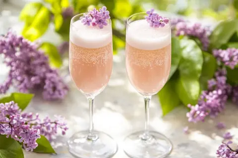 Två glas med rosa bubbel, dekorerade med syrenblommor. Perfekt för ett syrensirap recept.