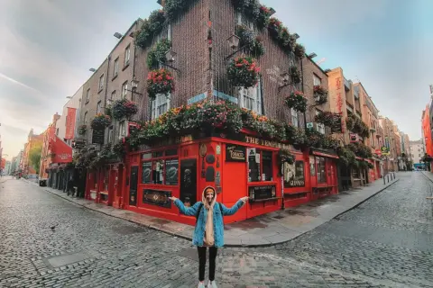Kobieta pozuje przed słynnym pubem The Temple Bar w Dublinie, stolicy Irlandii. Uliczka wybrukowana kocimi łbami.
