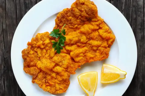 Ein knuspriges Wiener Schnitzel auf weißem Teller, garniert mit Petersilie und Zitronenspalten. Perfekt für einen herzhaften Genuss.