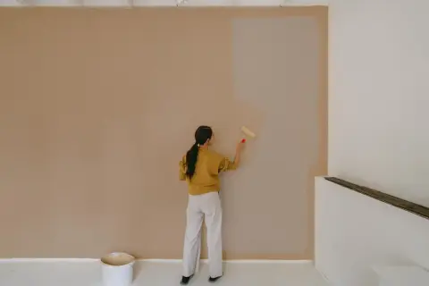 Frau streicht Wand mit neuer Farbe. Die Frage, wie lange braucht Wandfarbe zum trocknen, beschäftigt sie.