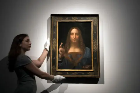 Kobieta w białych rękawiczkach prezentuje obraz "Zbawiciel świata". Ciekawe fakty o tym dziele Leonarda da Vinci.