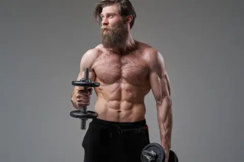 Mężczyzna z imponującą brodą wykonuje ćwiczenia na biceps, trzymając hantle do hammer curls.