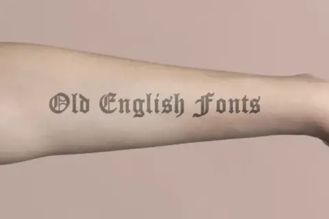 Ein Arm mit einem Tattoo-Schriftzug in Old English Fonts.