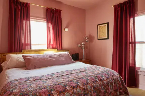 A bedroom with a large bed covered by a colorful quilt. Red curtains hang beside the bed, effectively creating a cozy nook and demonstrating how to hide a window behind a bed.