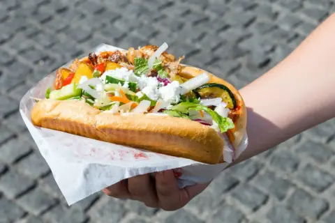 Kebab w picie z warzywami i serem feta, trzymany w dłoni.