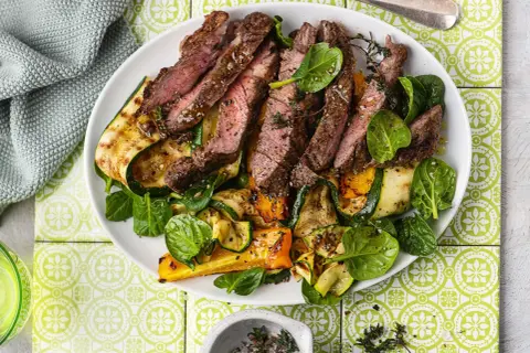 Pokrojony, soczysty sirloin steak z grillowanymi warzywami: cukinią, papryką i szpinakiem, udekorowany świeżym tymiankiem.