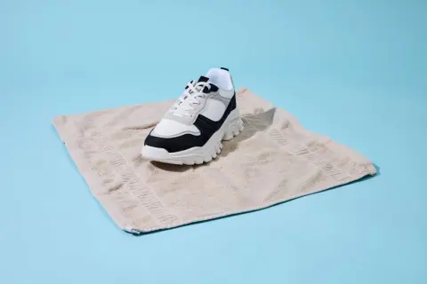 Sneaker bianco e nero su asciugamano beige, un metodo per asciugare scarpe bagnate dentro.