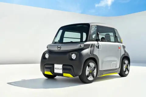 Najmniejszy Opel, Rocks-e, z żółtymi akcentami, prezentuje się nowocześnie na tle białej ściany i błękitnego nieba.