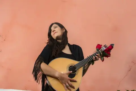 Młoda kobieta z gitarą, ozdobioną czerwonymi różami, przypomina duchem Amalię Rodrigues, legendę fado.
