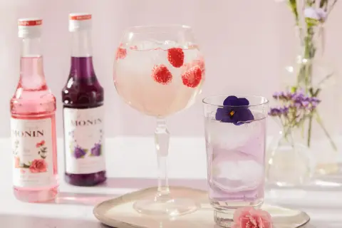 Dwa Monin syropy, malinowy drink w kielichu i fioletowy w szklance. Najprostsze drinki na lato.