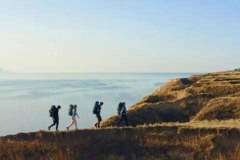 Fyra vandrare med ryggsäckar går längs en klippkant vid havet. En fantastisk vandring i Europa.