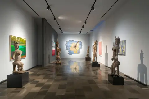 Osman Can Yerebakan's exhibition features striking wooden sculptures and vibrant paintings in a modern gallery space.