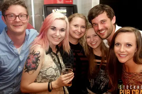Glada vänner på en pub crawl i Stockholm. En kvinna med rosa hår håller ett glas öl.