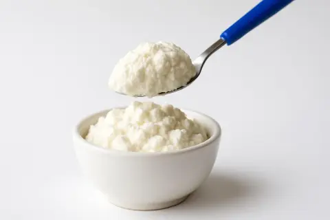 Ricotta fresca in una ciotola, con un cucchiaio che ne preleva una porzione. Un alimento leggero, ideale per chi controlla il colesterolo.