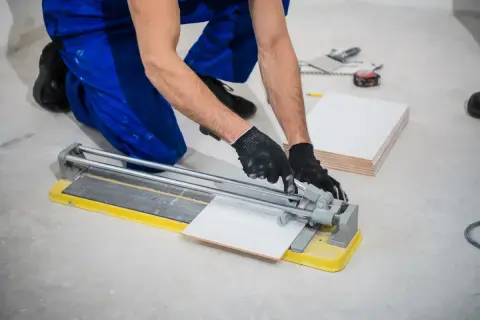 Ręce w rękawiczkach precyzyjnie tną gres 2 cm na płytkarskiej przecinarce.
