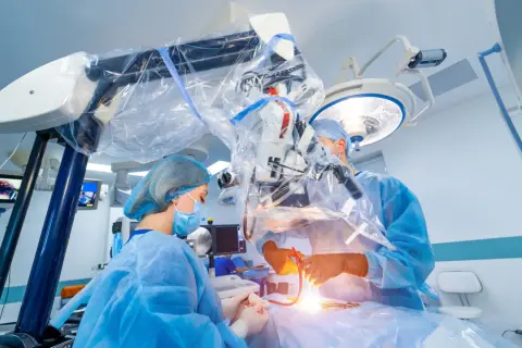 Chirurdzy w sterylnych strojach prowadzą skomplikowaną operację neurochirurgiczną pod mikroskopem.