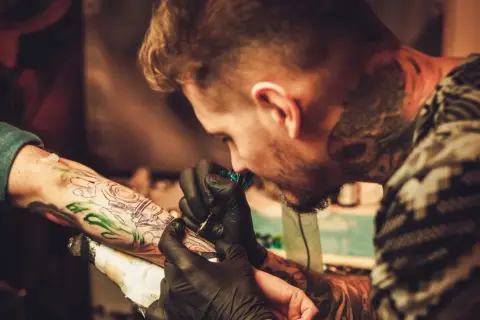 Ein Tätowierer mit vielen Rapper-Tattoos sticht einem Kunden ein neues Motiv auf den Arm.