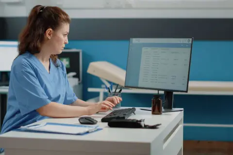 Rejestratorka medyczna kod zawodu pracuje przy komputerze, wprowadzając dane pacjentów.