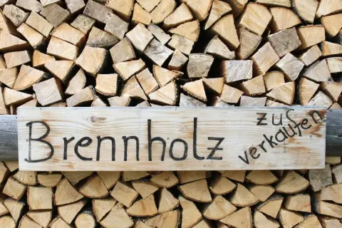 Holzstapel mit einem Schild "Brennholz zu verkaufen". Das Holz ist gespalten und bereit für den Winter, ob esche oder buche.