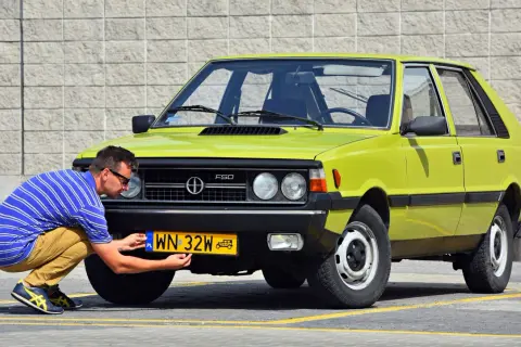 Mężczyzna przykręca żółtą tablicę rejestracyjną do zielonego Poloneza. Czy to auto ma już ile lat musi mieć auto na zabytek?