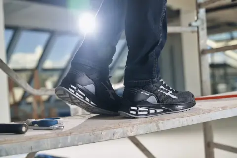 Scarpe guida U Power nere, con dettagli grigi e bianchi, indossate su un ponteggio. Perfette per chi lavora in cantiere.