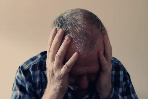 Mężczyzna w kratę trzyma się za głowę, jego twarz ukryta w dłoniach. Widać oznaki dekompensacji i przytłoczenia.
