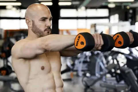 Uomo con manubri in palestra, parte di una scheda multifrequenza 4 giorni.