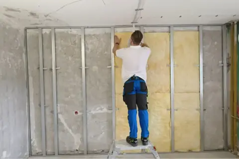 Pracownik montuje wełnę mineralną, by zapewnić wyciszenie sufitu od sąsiada. Metalowy stelaż i izolacja to klucz do ciszy.
