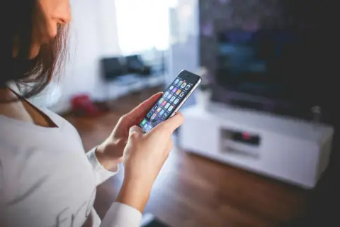 Kobieta przegląda aplikacje na telefonie, szukając sposobu, jak wyczyścić pamięć w telefonie, by zwolnić miejsce.
